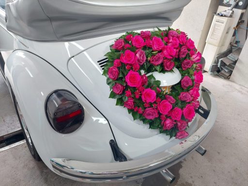 Weiße VW Käfer mit herzförmigem Blumenarrangement aus pinken Rosen.