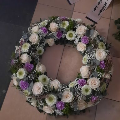 Kranz aus weißen Rosen, lila und grünen Blumen, mit grünen Blättern dekoriert.