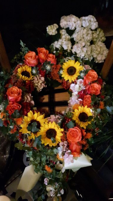 Bunte Blumenkranz mit Sonnenblumen, Rosen und kleinen weißen Blüten.