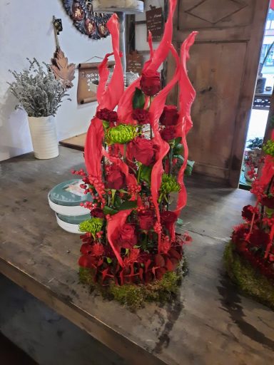 Rote Blumenarrangements mit grünen Akzenten auf einem Holz Tisch.