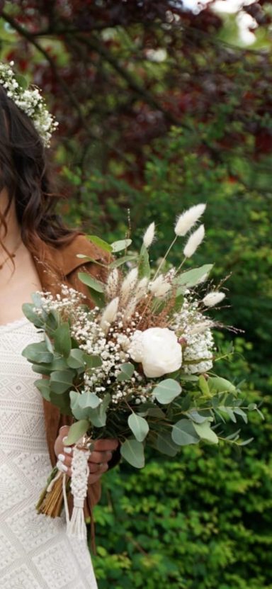 Braut hält einen Bouquet mit weißen Blumen und grünen Blättern.