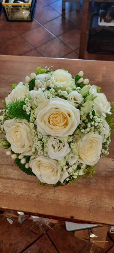 Weißer Blumenstrauß mit Rosen und kleinen weißen Blüten auf einem Holztisch.